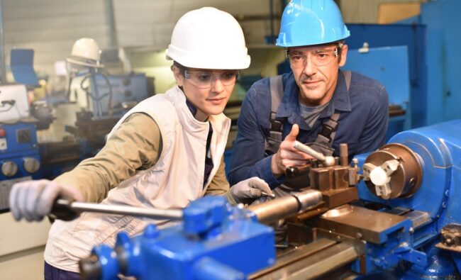 Metal-worker-teaching-trainee-on-machine-use
